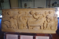 Front of a child's sarcophagus depicting, on the left, the child at school, and on the right, the child's moment of death. From the 2nd century CE.