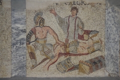 Detail of the gladiator mosaic in the Museo Archeologico al Teatro Romano. The gladiator Caecrops has been killed by a thraex and is loaded on to a litter.