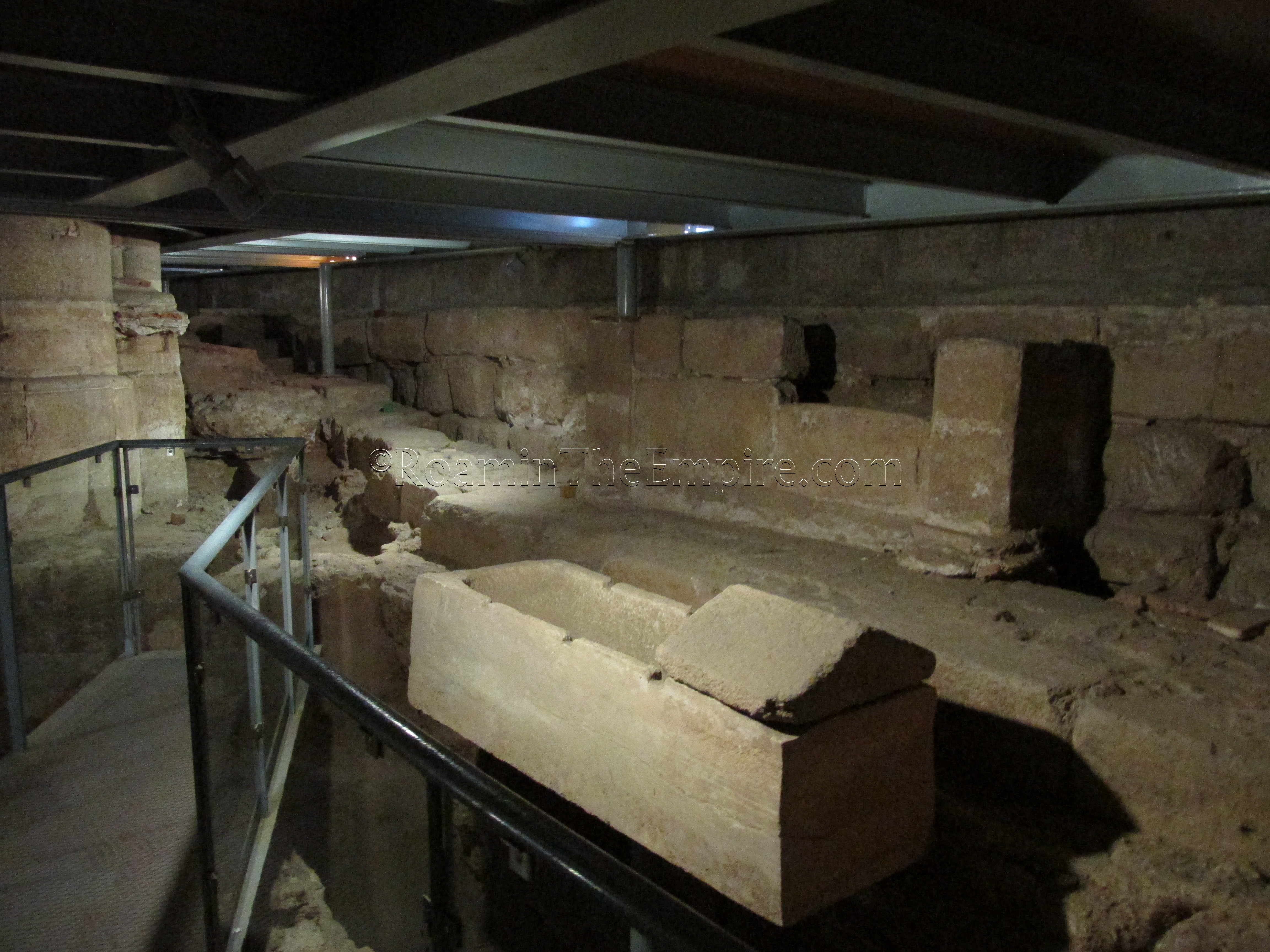 Part of the Roman house's bath and cistern on the left, sarcophagus and early basilica wall on the right.